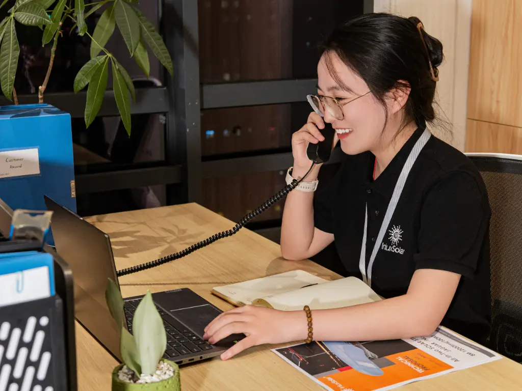 Smiling employee answering phone call at computer desk with project documents on desktop